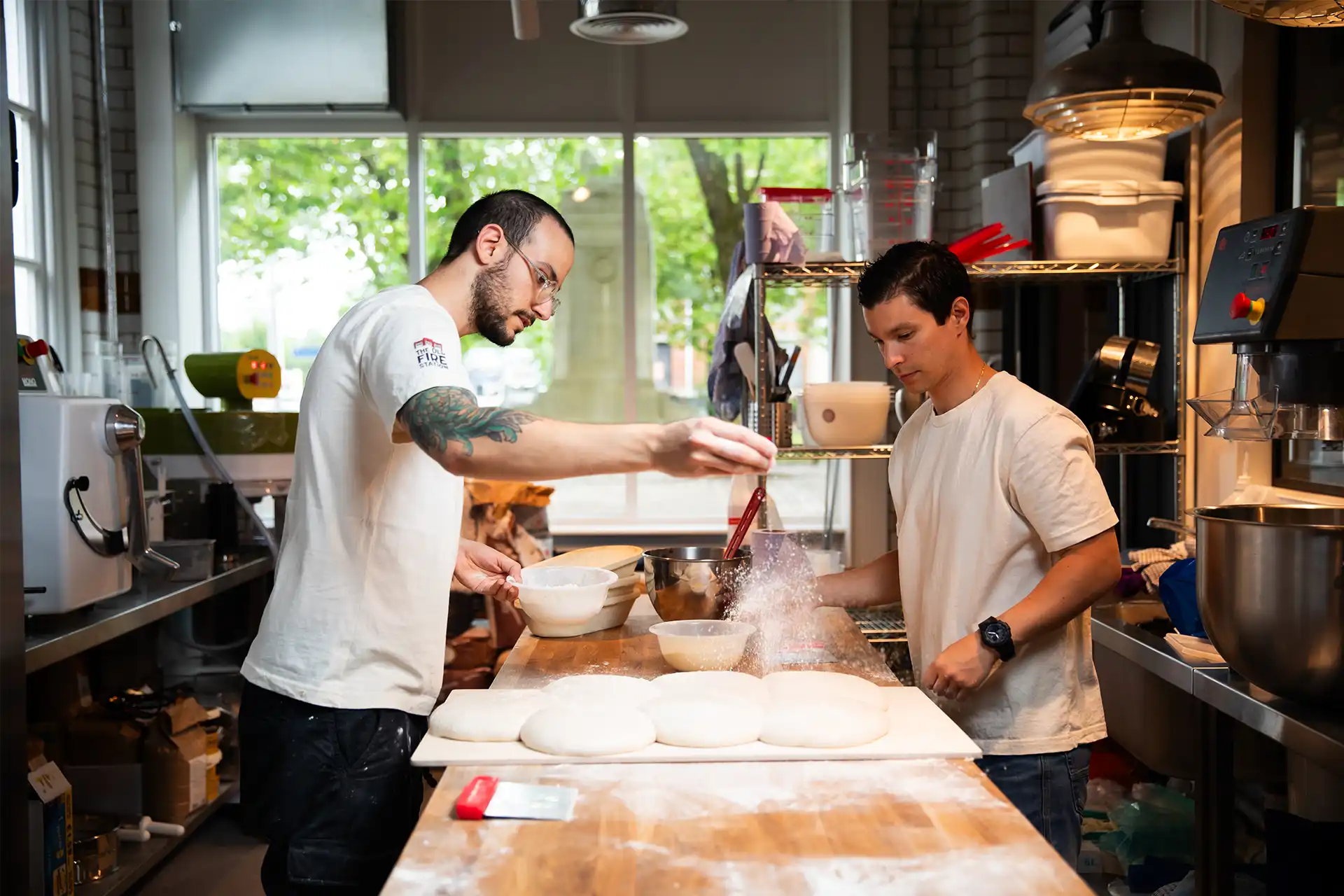 Two male beakers kneading dough in a kitchen